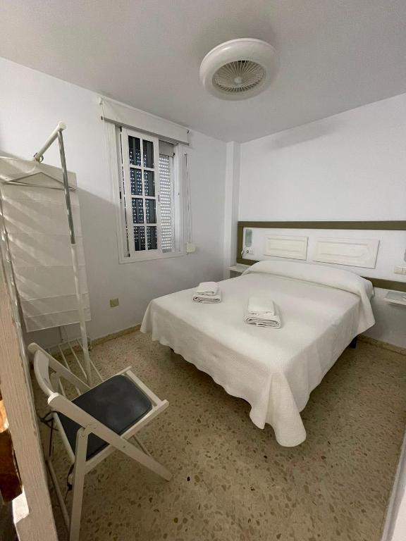 a white bedroom with a bed and a chair at Sanpau in Vejer de la Frontera