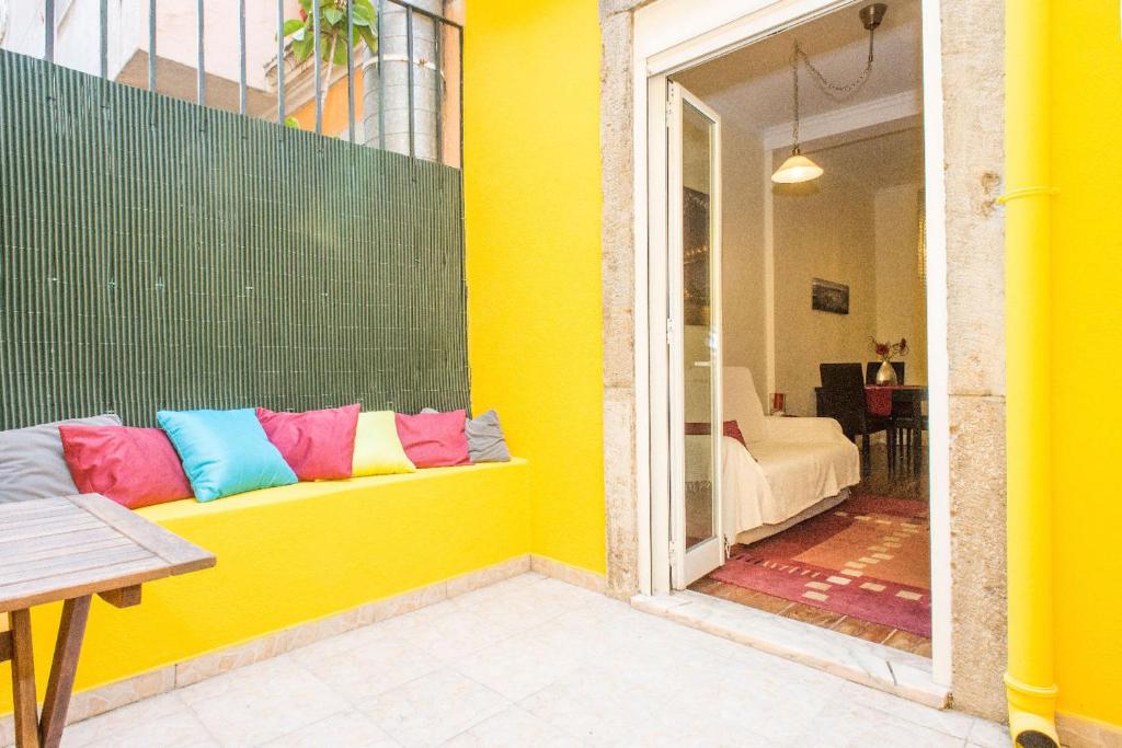 a yellow wall with a bench with colorful pillows on it at Find Me Inn Alcantara in Lisbon