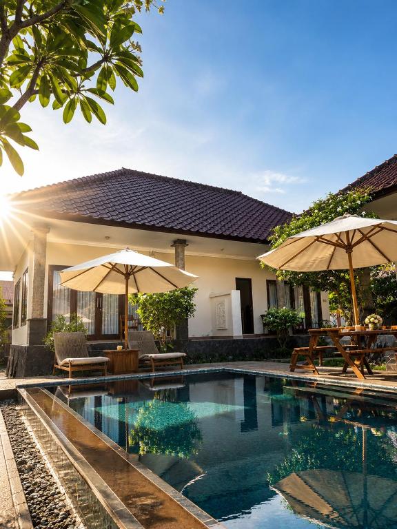 a swimming pool with two umbrellas and a house at Noble Bali Diving Resort Tulamben in Tulamben