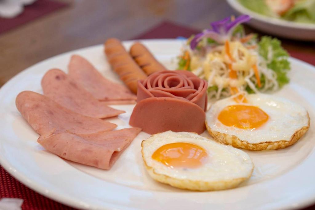 A plated breakfast of fried eggs, sausages, luncheon meat, and salad.