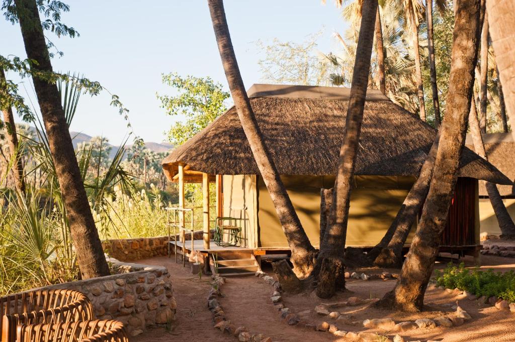 a hut with a thatched roof in the middle of trees at Omarunga Epupa-Falls Camp in Epupa