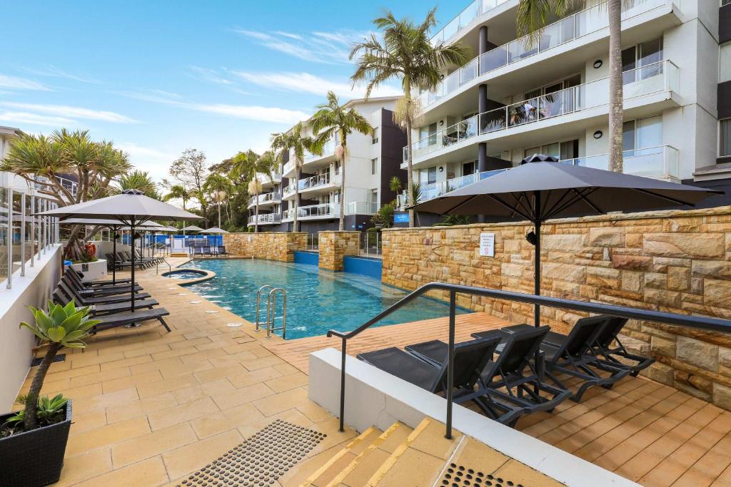 a swimming pool with chairs and umbrellas next to a building at Solara at Aqua Mantra in Nelson Bay
