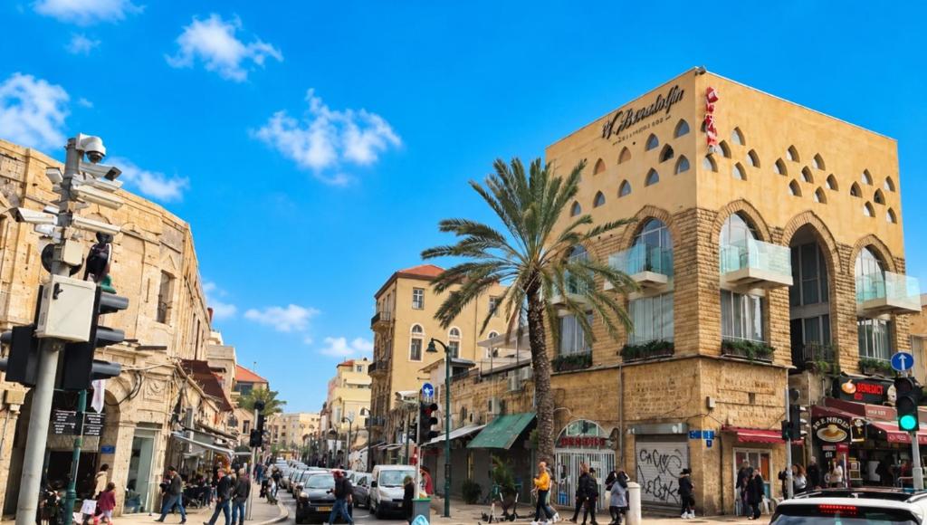 a busy city street with a building and a palm tree at Safra - Hotel rooms in Tel Aviv