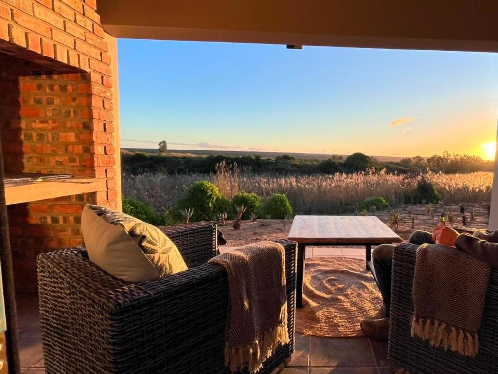 a patio with wicker chairs and a table with the sunset at Olive Grove Addo in Addo