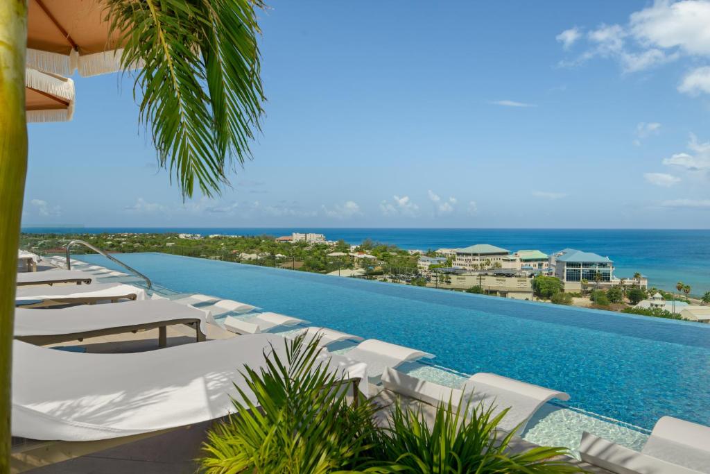 a pool with white lounge chairs and the ocean at ONE GT Grand Cayman in George Town
