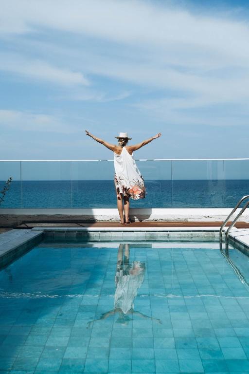 a woman standing by a swimming pool with her arms outstretched at Villa Akroyiali - Seafront Serenity with Shared Pool in Pachyammos