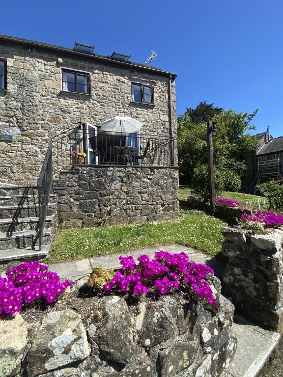 a stone house with purple flowers in front of it at Saddle Cottage in Penzance