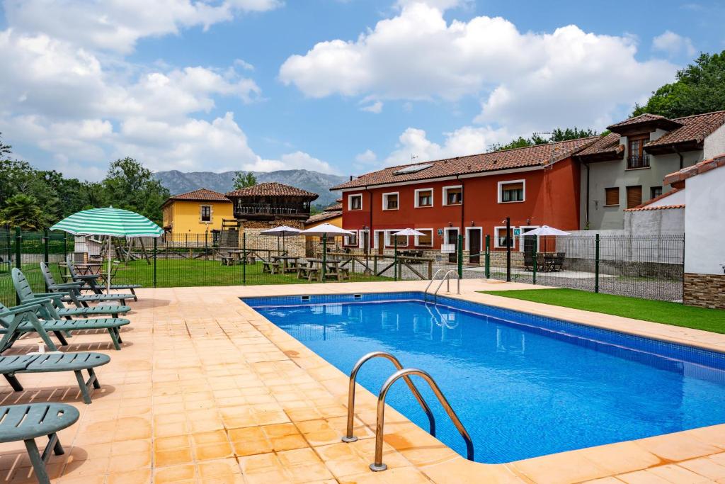 a pool with chairs and umbrellas next to a building at Huerta El Pozu in Soto de las Dueñas