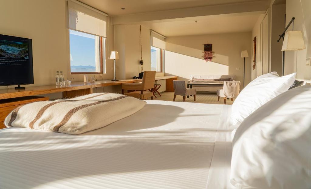 a bedroom with a large white bed and a desk at Hotel Patagonico in Puerto Varas