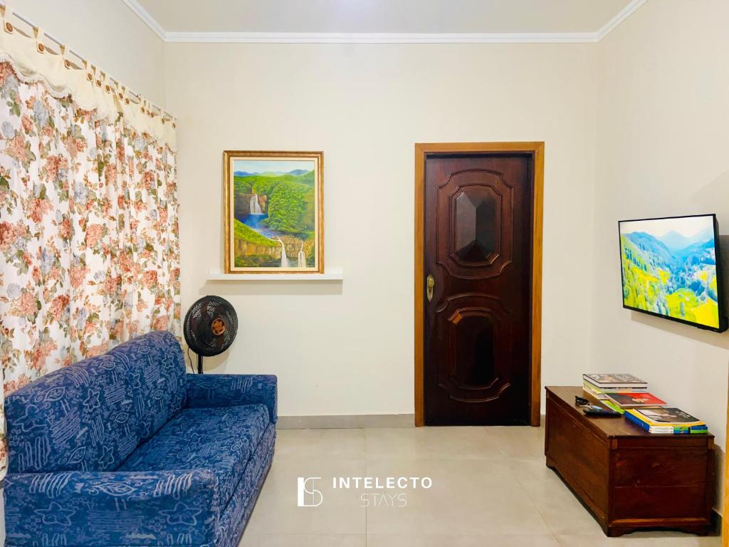 a living room with a blue couch and a wooden door at Casa Central Px Matriz c/ Churrasqueira, 2 Suítes in Poços de Caldas