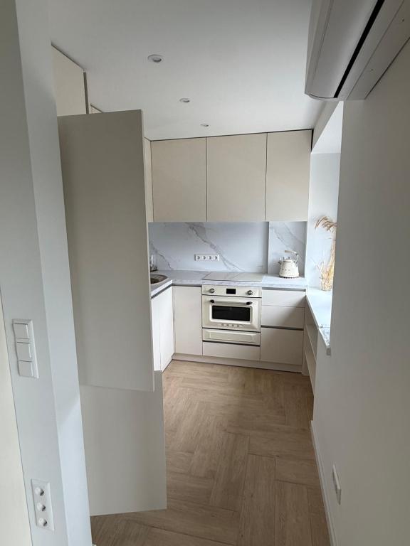 a kitchen with white cabinets and a wooden floor at Greta Apartment in Alytus