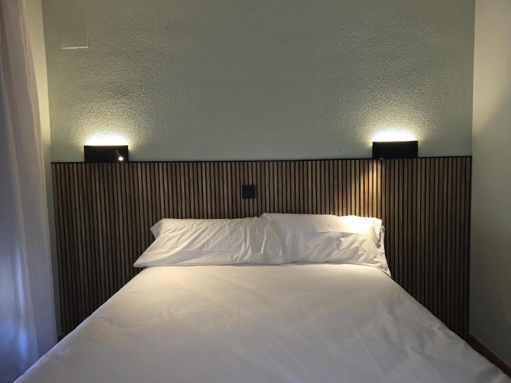 a bed with white sheets and two lights above it at Hostal La Cigüeña in El Espinar