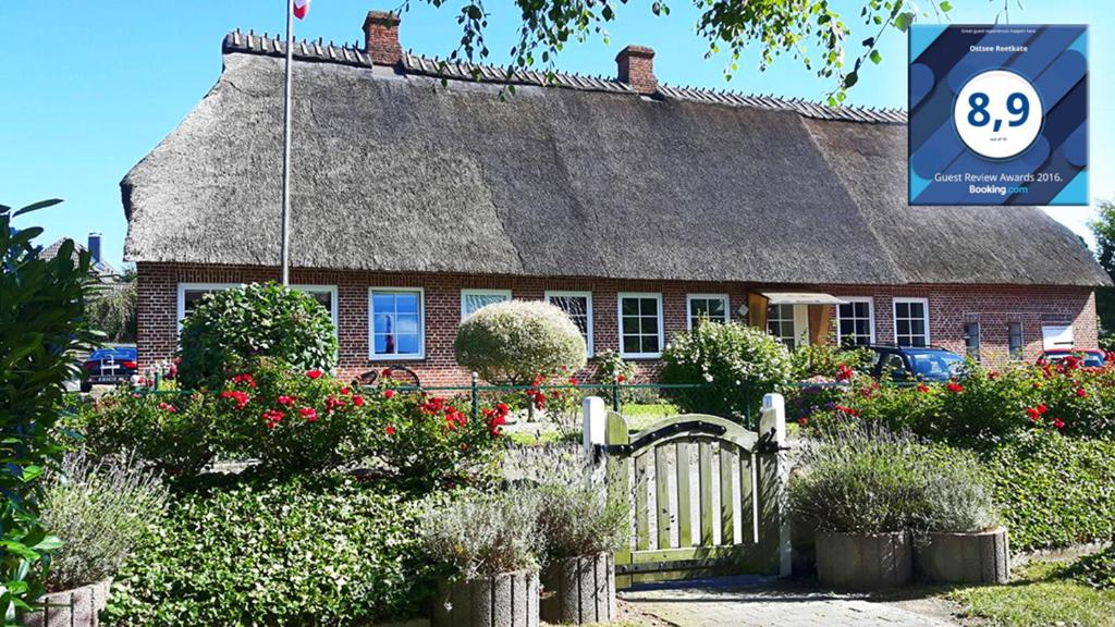 a house with a thatched roof with a gate and flowers at Ostsee Reetkate in Langballig