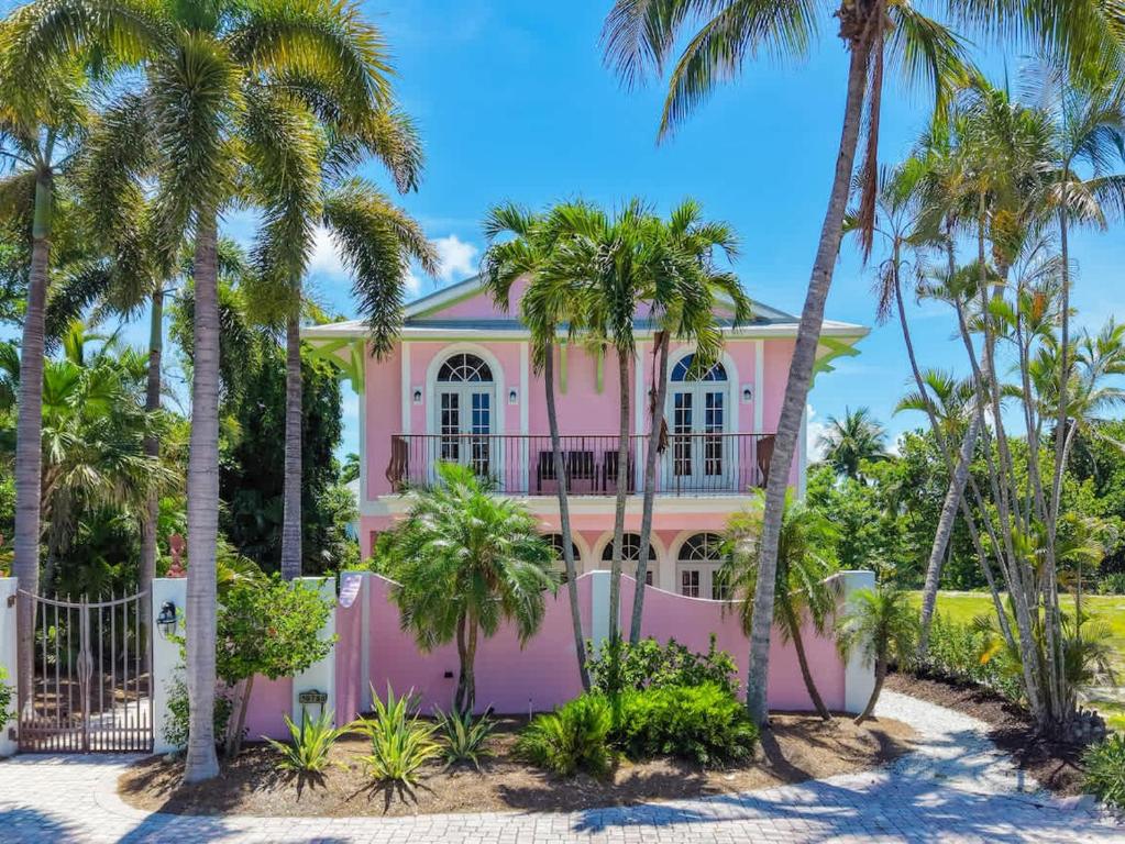 a pink house with palm trees in front of it at Waterfront Pink House with Private Dock & Pool in Captiva