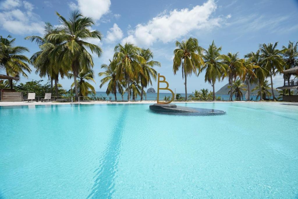 a large swimming pool with palm trees in the background at Suite Caraïbe vue mer in Le Diamant