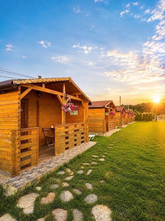 a row of wooden lodges in a field with the sunset at Casa Fericirii in Cârțișoara