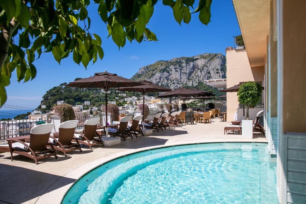 a pool on the roof of a hotel with chairs and umbrellas at Capri Tiberio Palace - The Leading Hotels of the World in Capri