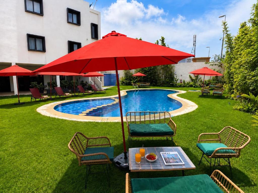 ein Tisch mit einem roten Sonnenschirm neben einem Pool in der Unterkunft Hotel Ben Batouta - Tanger in Tangier