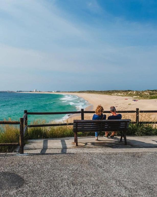 two people sitting on a bench near the beach at Estrela do Mar - 100m da praia in Peniche