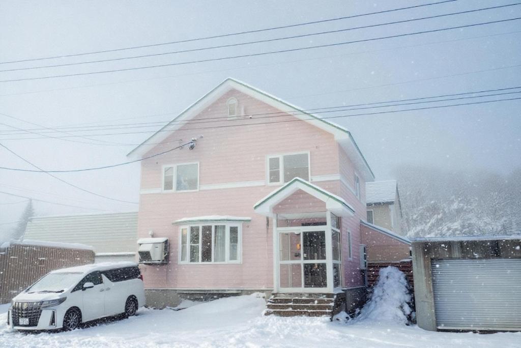 a pink house with a car parked in the snow at Niseko Pink house in Kutchan