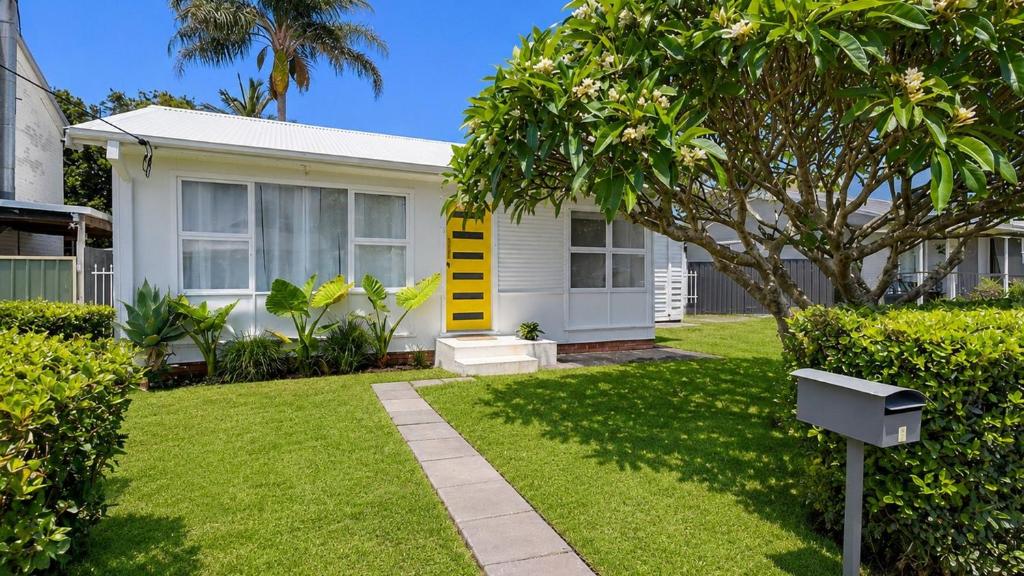 a white house with a tree in a yard at Frangipani Hideaway in Budgewoi