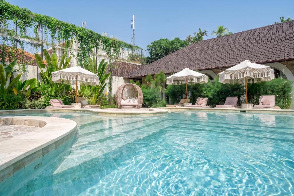 a swimming pool with chairs and umbrellas at Maison Boheme Modern Apartment & Villa with Pool in Sanur in Sanur