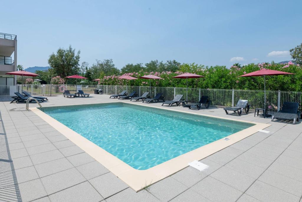 a swimming pool with chairs and umbrellas at Comfort Aparthotel Cannes Mandelieu in Mandelieu-La Napoule