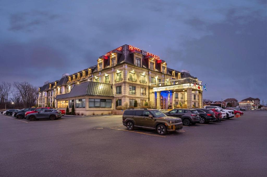 ein großes Gebäude mit auf einem Parkplatz abgestellten Autos in der Unterkunft Hotel Brossard, an Ascend Collection Hotel in Brossard