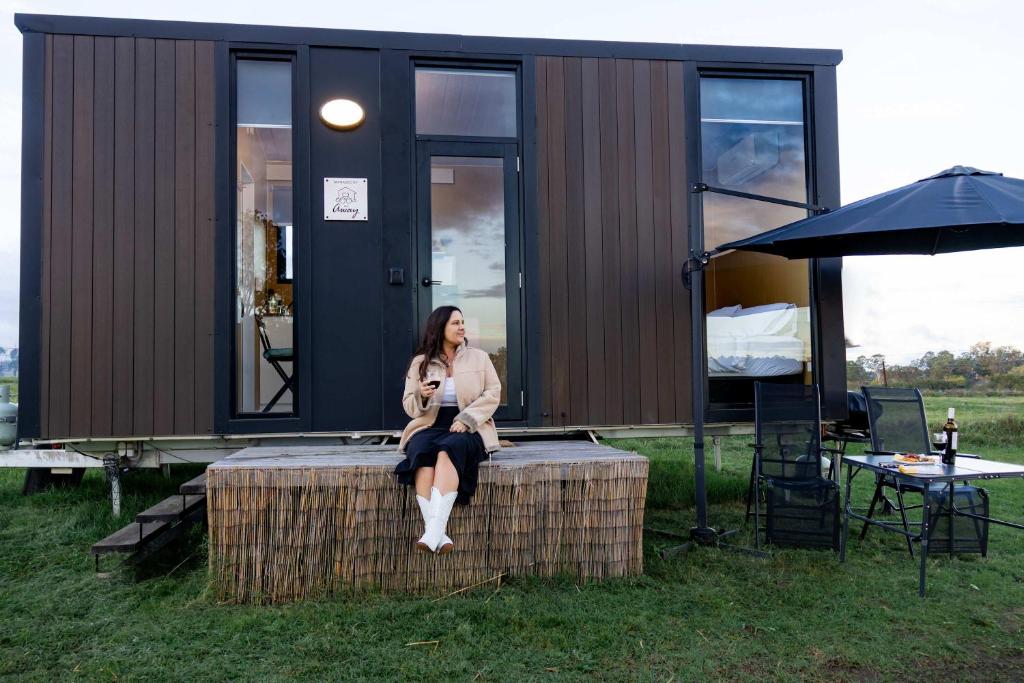 a woman sitting on a table in front of a tiny house at Pasture and Paws by Tiny Away in Leeville