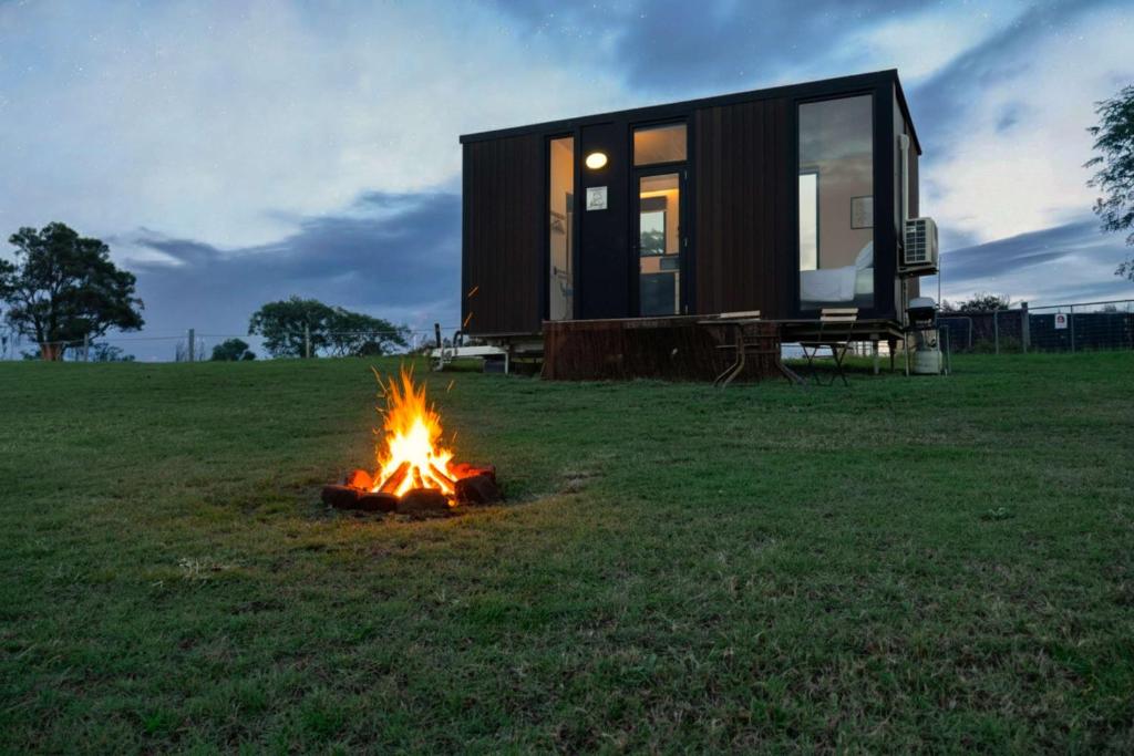 a tiny house sitting in a field with a fire at Hills and Herds by Tiny Away in Shannon Brook