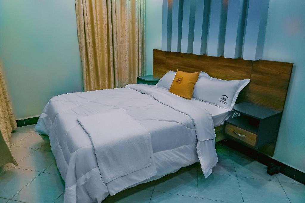 a bedroom with a large bed with white sheets and yellow pillows at Neriah Suites in Kabale