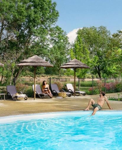 a man laying on the edge of a swimming pool at Camping Onlycamp les Cochards in Seigy