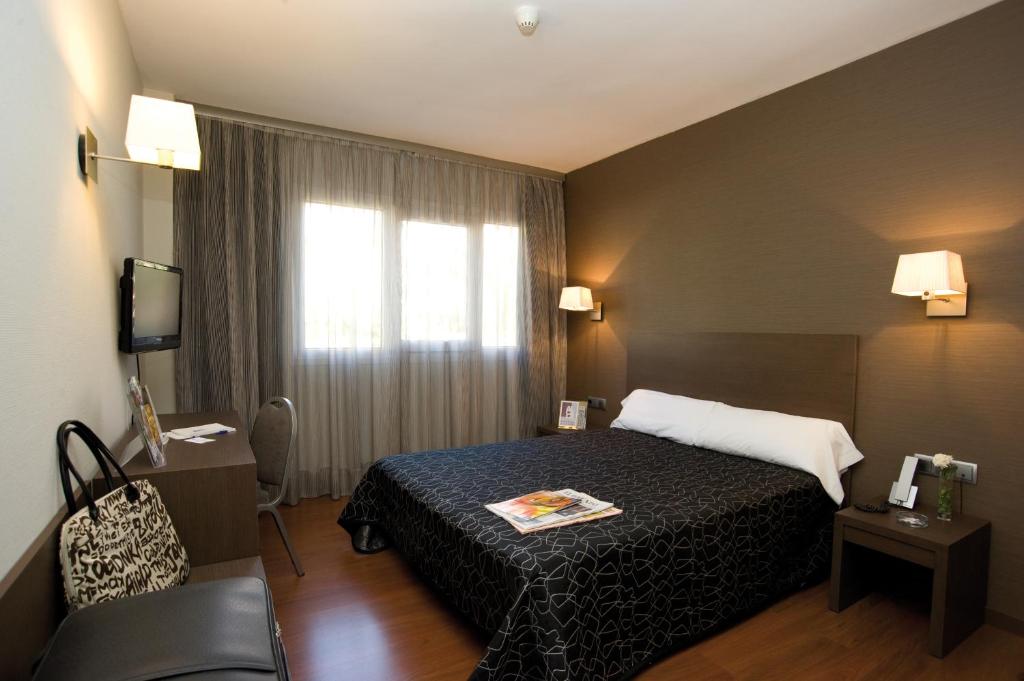 a hotel room with a bed, chair, and nightstand at Hotel Cisneros in Alcalá de Henares