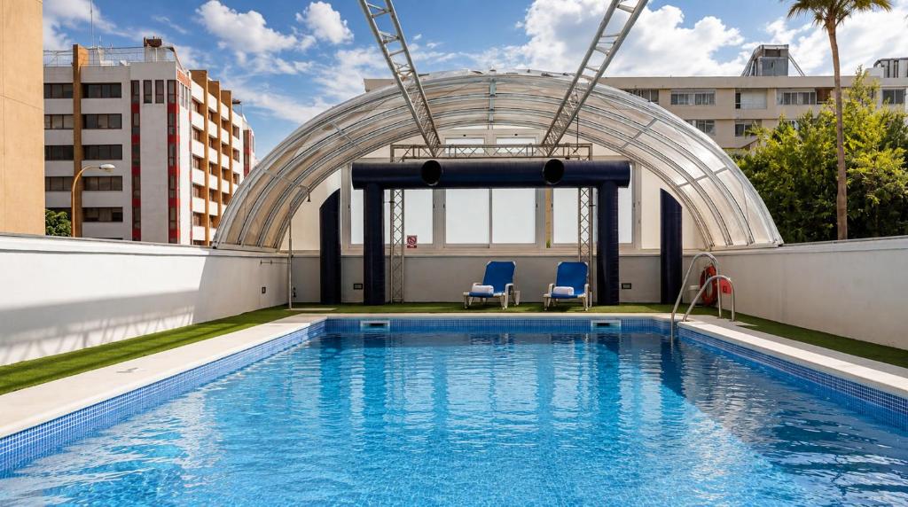 a swimming pool on the roof of a building with two blue chairs at Vértice Sevilla in Seville