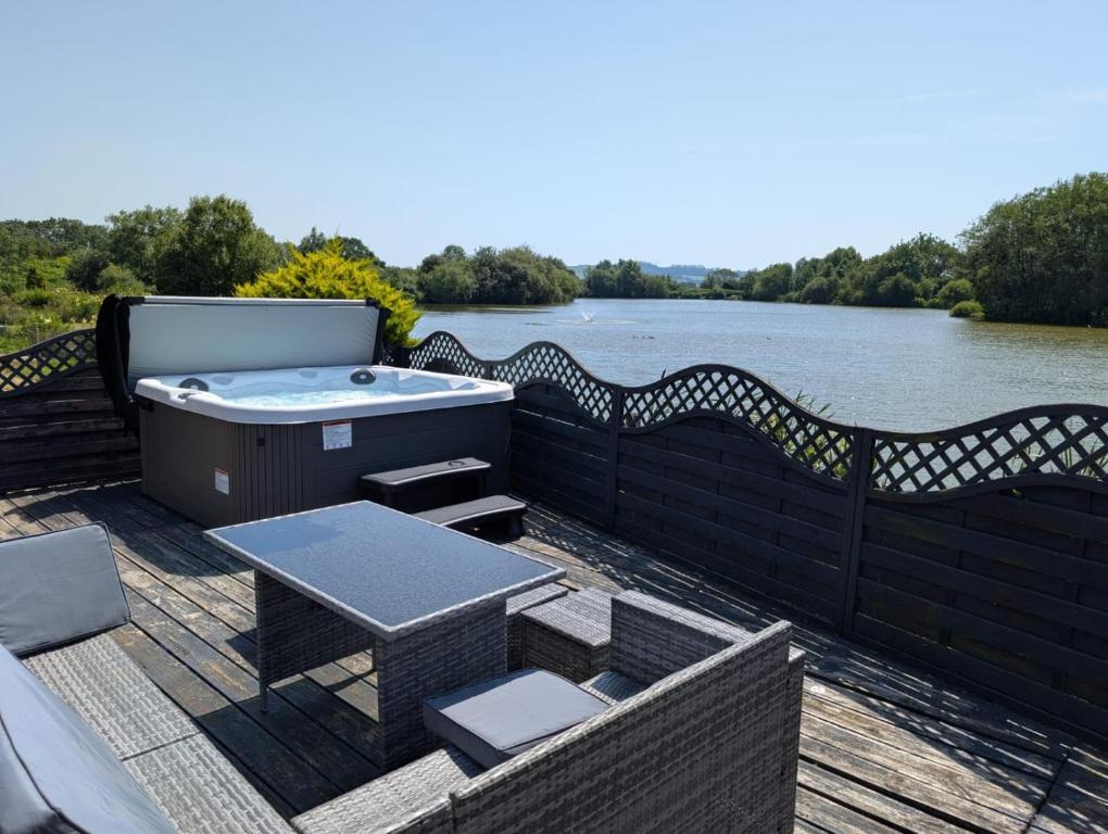 a hot tub on a deck next to a river at Lakefront Lodge with Hot Tub - Aylesbury Lodge in Shepton Mallet