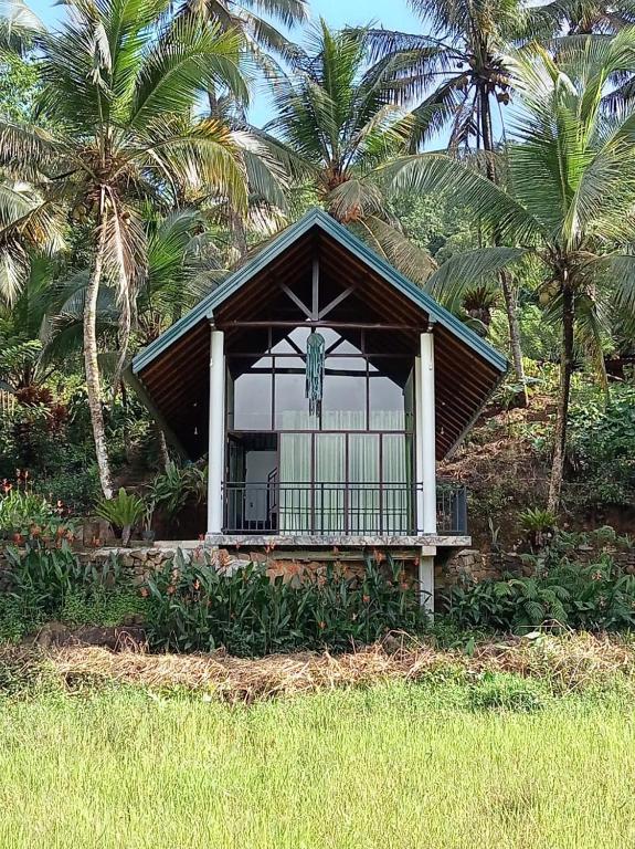 a small building with a statue in front of palm trees at Rainforest Nature Resort - Sinharaja in Deniyaya