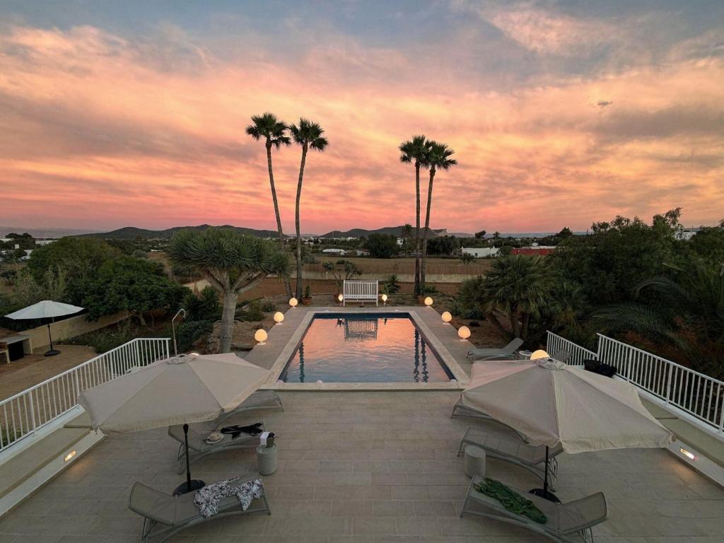 a swimming pool with two umbrellas and palm trees at Can Paola in Sant Josep