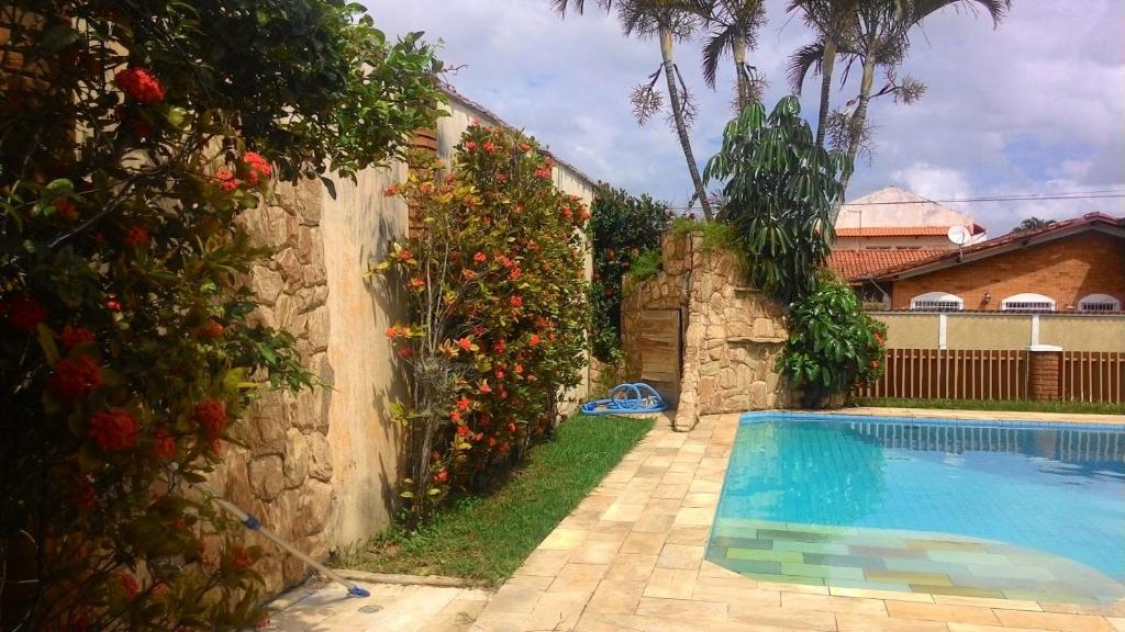 a swimming pool next to a stone wall with flowers at Recanto Praia Peruibe in Peruíbe