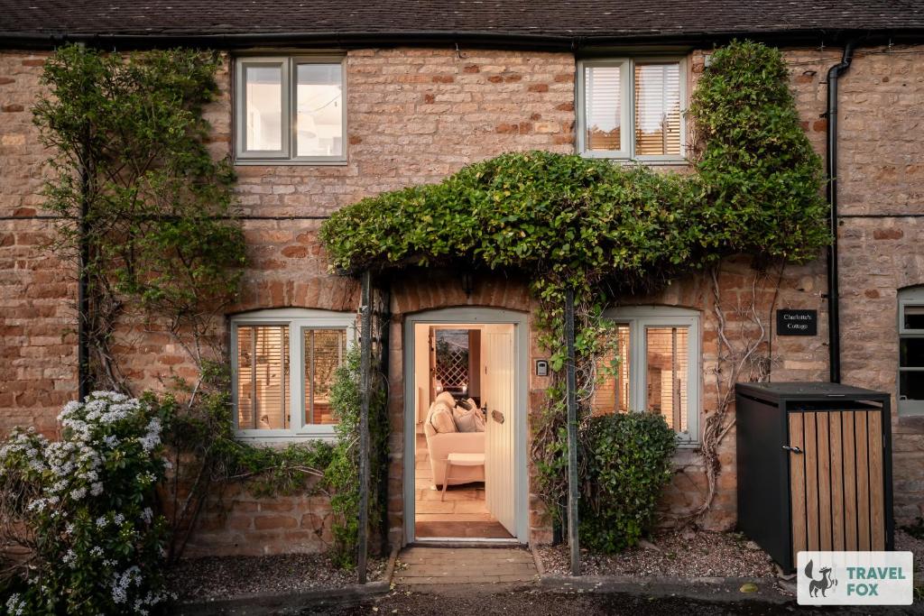a brick house with two people sitting in the doorway at Charlotte's Cottage, a Charming Cotswolds Getaway in Adlestrop