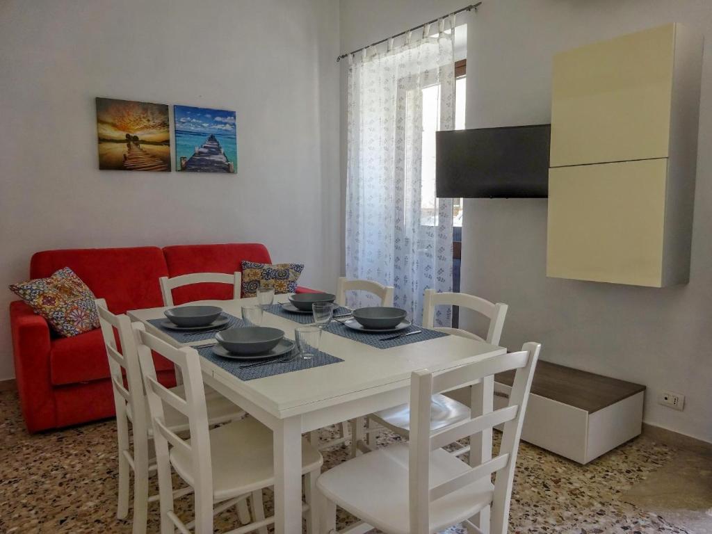 a white dining room table with white chairs and a red couch at Maison Vivian Apartment in Marzamemi