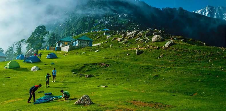 a group of people on a green hill with tents at Magic Valley Devroopa Trek - Pickup and drop to New Delhi in Kulu