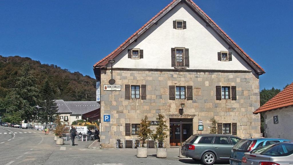 un gran edificio de piedra con coches aparcados en un aparcamiento en Posada de Roncesvalles, en Roncesvalles