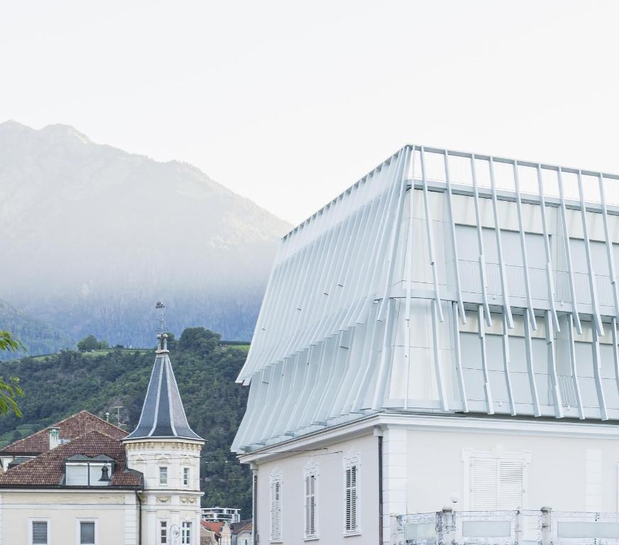 ein großes weißes Gebäude neben einem Gebäude mit einem Turm in der Unterkunft Hotel Aurora in Meran
