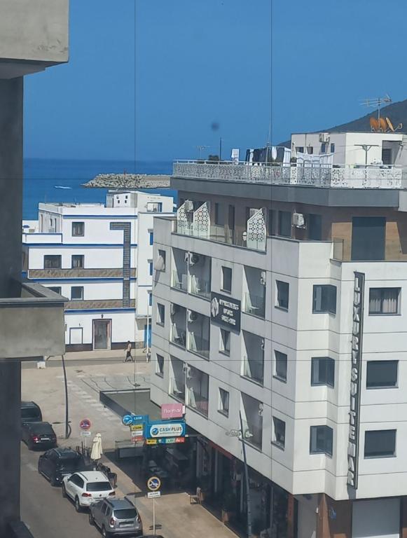 a white building with cars parked in a parking lot at Resicence jaouharat zarkaa in M'diq
