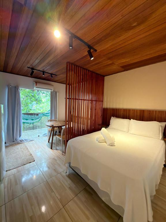 a bedroom with a large white bed and a table at Pituba Vile - Apartamento Jardim in Itacaré