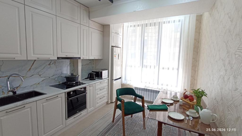 a kitchen with white cabinets and a table with a green chair at Osh apartment in Osh