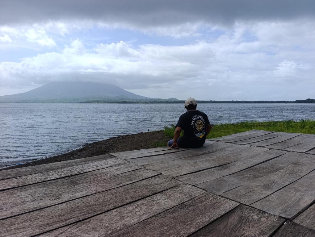 a man sitting on a dock looking at the water at Kencho's Beach House-Sunset & Beachside stay in Ometepe in El Perú
