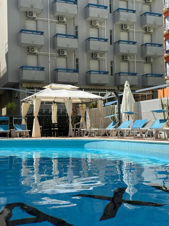 a swimming pool with a white umbrella and chairs and a building at Hotel Marea con Piscina NUOVA GESTIONE in Cattolica