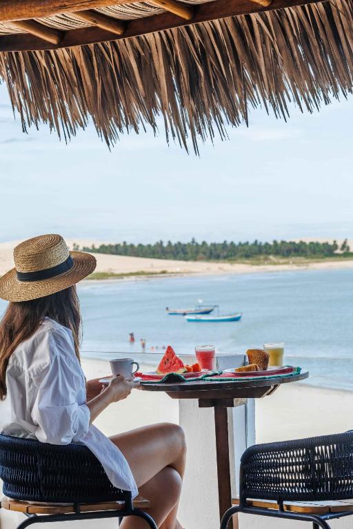 a woman sitting at a table with a tray of food on the beach at Vila Gallina Pousada in Jericoacoara