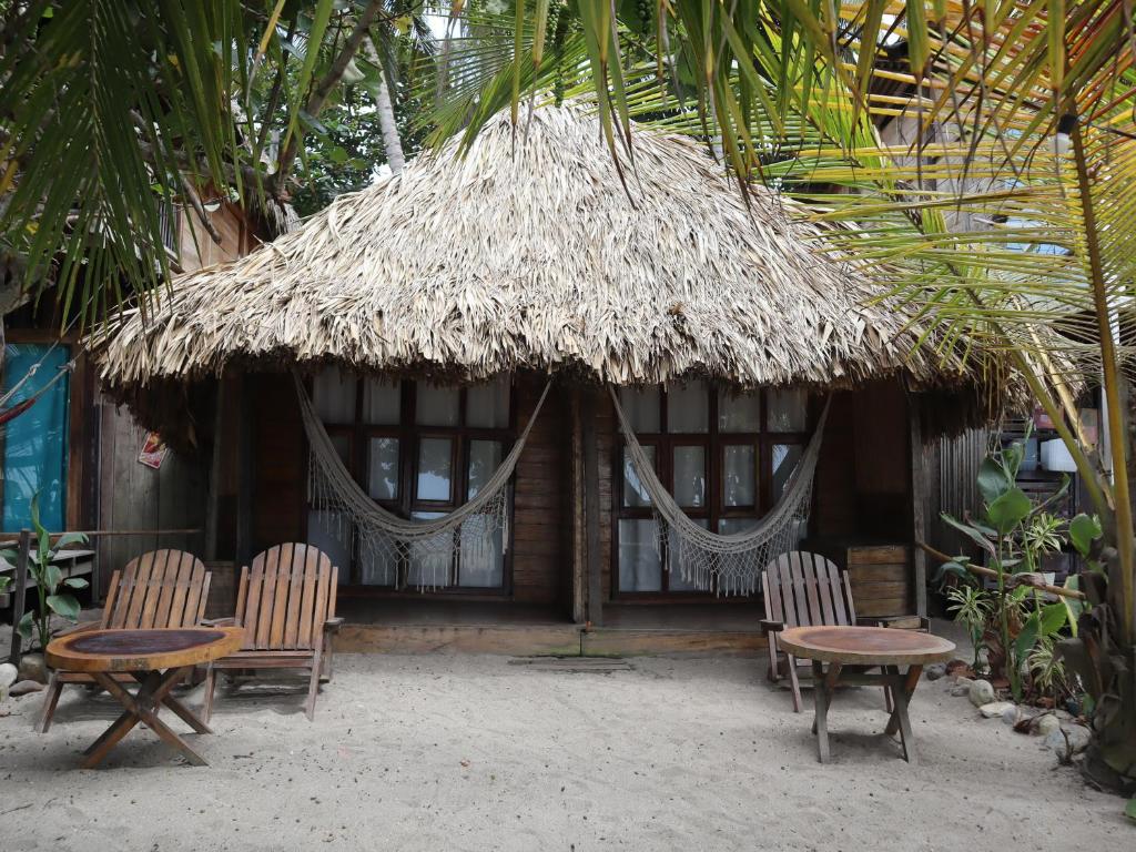a hut with chairs and a table and a straw umbrella at Chill and Surf Mendihuaca in Santa Marta
